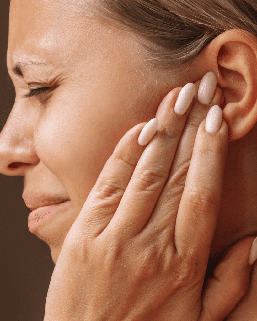 Donna che si tocca un orecchio con espressione di dolore, possibile fastidio o infezione all’orecchio