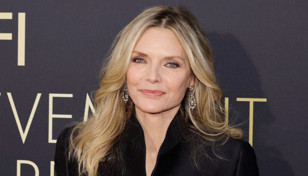 Michelle Pfeiffer sorride e posa sul red carpet durante un evento di gala, indossando un elegante abito da sera