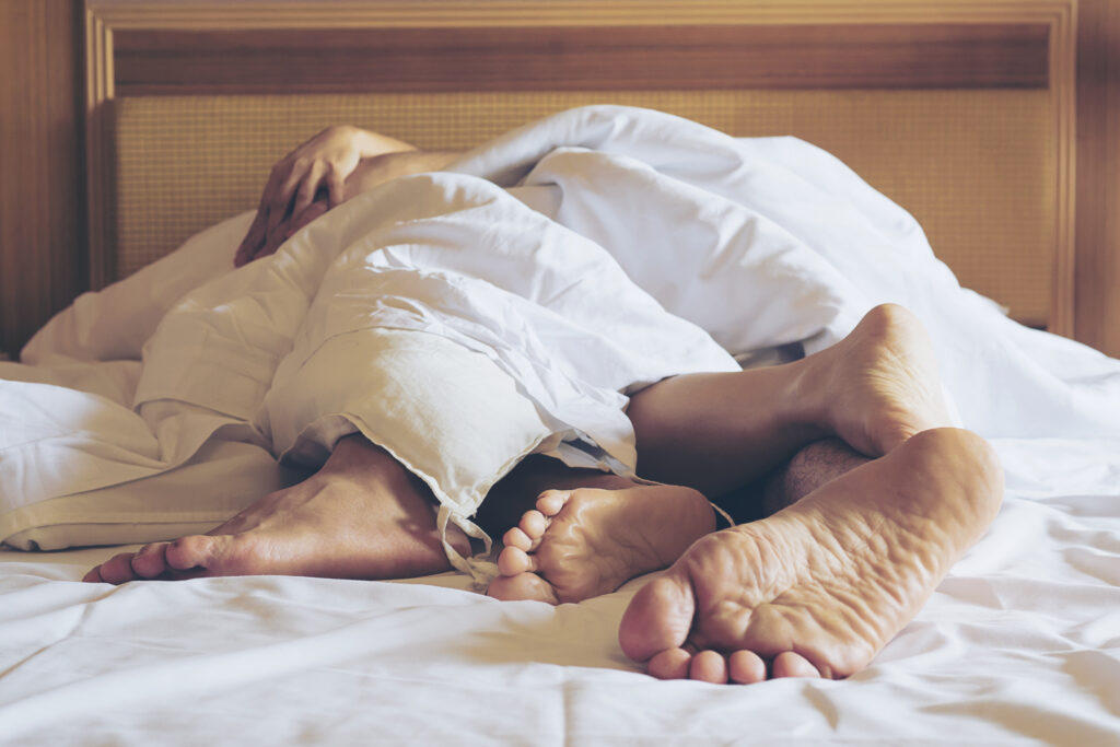 Coppia distesa su un letto bianco in camera d’hotel, primi piani dei piedi