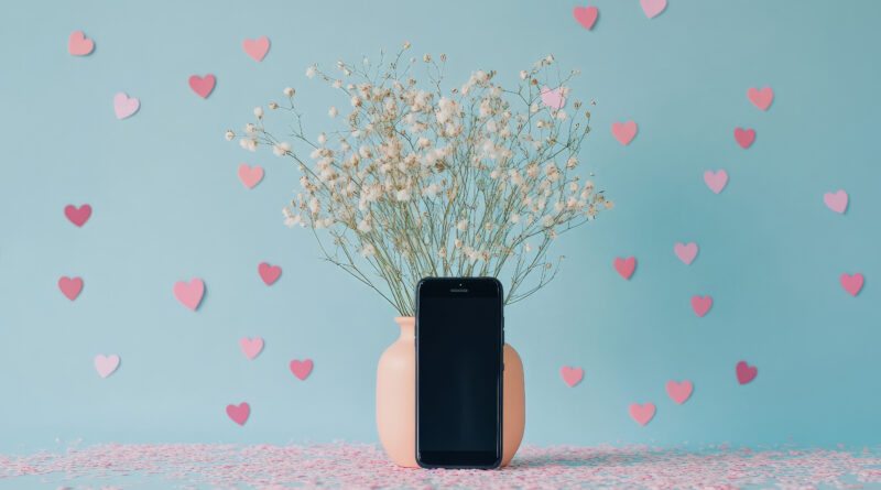 Vaso pesca con fiori di gypsophila accanto a un telefono nero su sfondo azzurro con cuori rosa