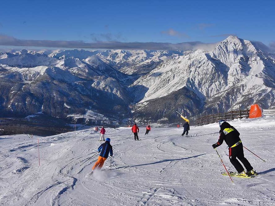 Sciatori sulle piste di Sestriere con panorama delle Alpi